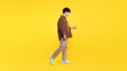 Sad guy using cell phone while walking over yellow background