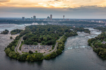 Aerial panorama of Niagara Falls with tall buildings across Niagara River at sunset. Warm cloudscape