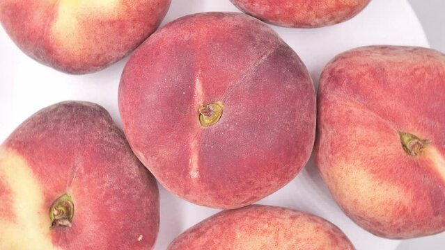Ripe flat peaches, rotating clockwise on a white background. Concept of fruit, healthy eating, seasonal food, ready to eat, vitamins and minerals. Real time video.