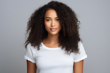 Young beautiful afroamerican woman model with dark curly hair in white t-shirt posing on light grey background