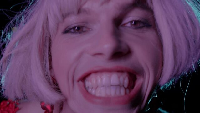 Drag Queen in blonde wig grimacing on camera in neon light