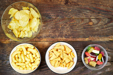 birthday or christmas, new year's party concept, a bowls of different chips and candies on  wooden table - obrazy, fototapety, plakaty