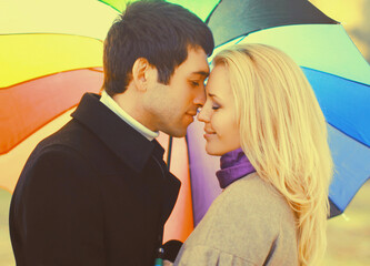 Happy loving young couple kissing and hugging under colorful umbrella in autumn park on warm sunny day