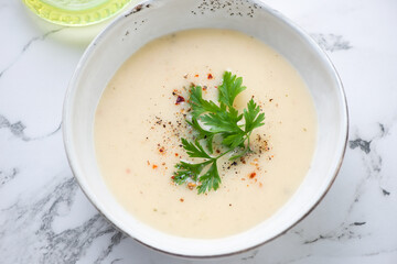 Bowl of cheese cream-soup topped with fresh parsley, elevated view on a white marble background, middle closeup