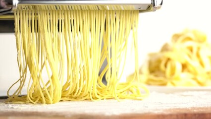 Production of pasta on a pasta cutting machine.  Fresh handmade pasta coming out from machine, close up. Traditional Italian homemade pasta being made on the machine for cutting dough
