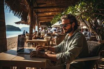 Obraz na płótnie Canvas Young freelancer working on laptop from tropical destination. Man sitting under palm trees on beach.