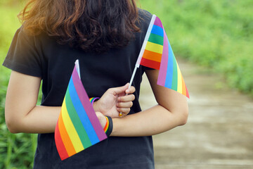 Asian woman wearing black shirt holding rainbow flag2 crossed at the back on her wrist she wears a black wristband with the message pride and a rainbow wristband. Symbol of lgbt pride