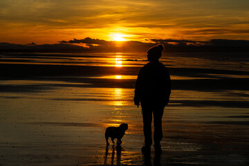 Woman and dog silhouetted on beach at sunset