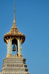 An ornate Thai temple bell tower with a golden roof and colorful details, stands against a clear blue sky.