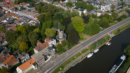 Fototapeta na wymiar Aerial drone shot of treetops, trees, houses and shop rooftops of Dutch city Gouda centre with historic building het slot windmill with nieuwe veerstal road and Hollandsche Ijssel on clear sunny day
