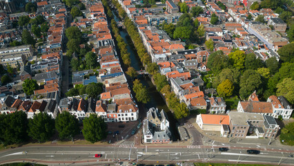 Aerial drone shot of treetops, trees, houses and shop rooftops of Dutch city Gouda centre with historic building het Tolhuis or toll house with nieuwe veerstal road on clear sunny day