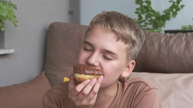 A cute guy eats a donut, enjoying the sweet taste of chocolate glaze.