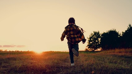 Child girl runs through green grass in sun. Childhood dream happiness concept. Joyful little girl running at sunset. Kid is running across field. Happy child playing in nature. Happy family. Dream kid