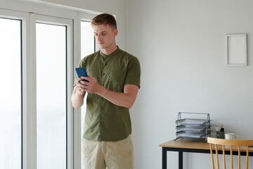 Fototapeta na wymiar Frowning young man checking text messages from coworkers in smartphone