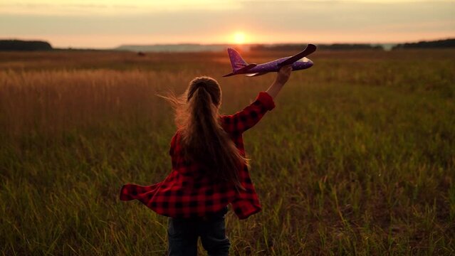 Happy kid girl runs with toy airplane on field in sunset light. Child play toy airplane. Kid aviator dreams of flying becoming pilot. Little girl child wants to become pilot astronaut sky Slow motion