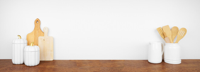 Autumn theme kitchenware, utensils and decor on a wood shelf or counter. Banner against a white wall background with copy space. Fall kitchen, home cooking concept.