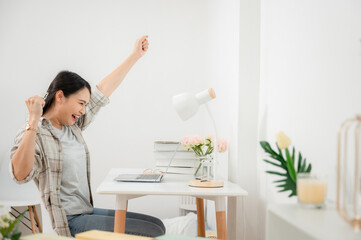 Portrait of happy freelance Asian woman working at home feeling excited and extremely happy with laptop.