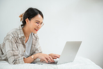 Portrait of Happy Asian freelancer talking remotely online on laptop at her bed at home.