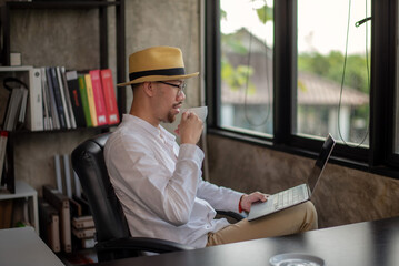 Businessman in casual clothes relaxing with coffee while working on laptop. Thoughtful about project plan.