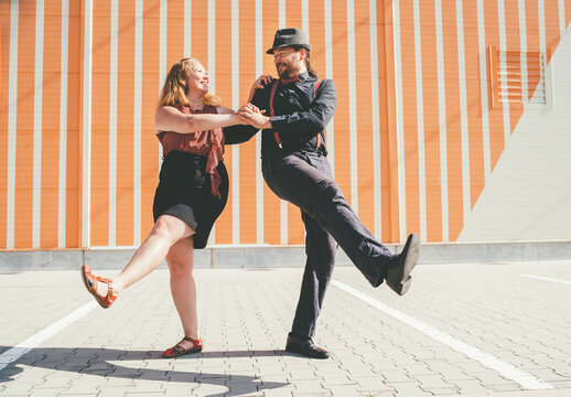 Cheerful couple dancing a retro swing dance to jazz music which was very popular during West Coast Swing era in 1920-40s. They are smiling to each other next to striped wall background.