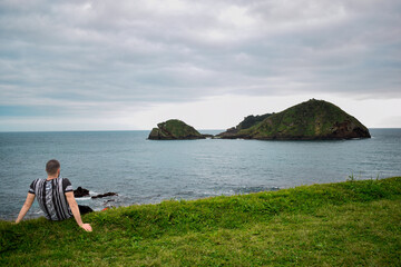Fototapeta premium Young man sitting in meadow watching the sea