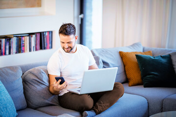 Handsome man sitting at home and using a laptop and mobile phone for work