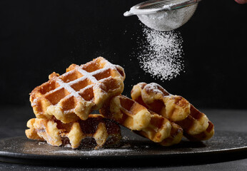 A stack of baked Belgian waffles sprinkled with powdered sugar