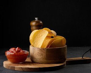 Potato chips in a wooden bowl and a bowl of sauce on a black table, snack