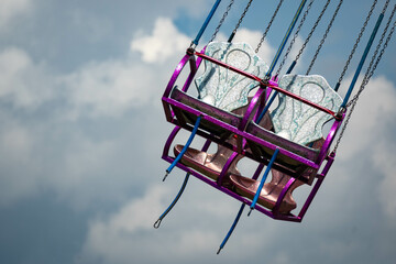 bright lilac carved beautiful seats of an air carousel on chains in an amusement park high above the ground against a blue sky background
