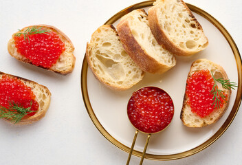 Sandwiches with red caviar and bread in a round plate on a white table, top view