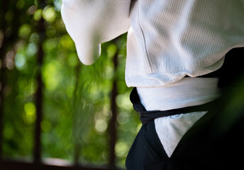 side view of the belt of a man in a white uvagi jacket and a black hakama at aikido training on a...