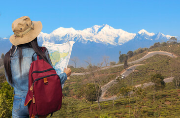 A Female tourist with map in hand enjoys view of the Himalayan landscape with view of the Kanchenjunga Himalaya range at Tichuley, Darjeeling, India