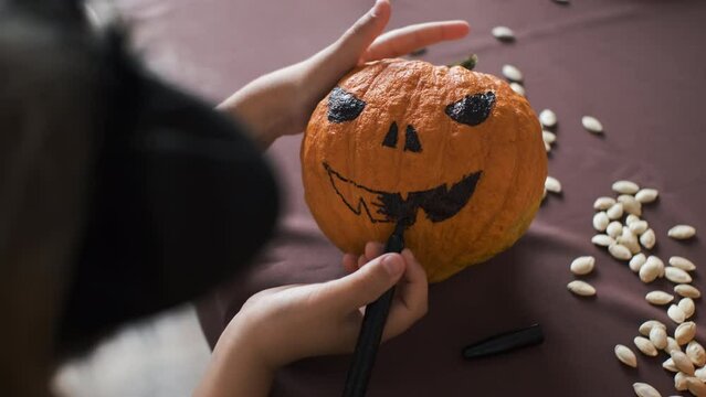 Close-up of little girl painting face on pumpkin, Halloween preparation concept