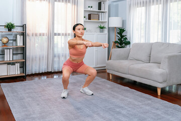 Fototapeta na wymiar Vigorous energetic woman doing exercise at home. Young athletic asian woman strength and endurance training session as home workout routine with squat.