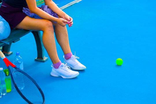 A young girl tennis player is resting while sitting on a bench in between games 