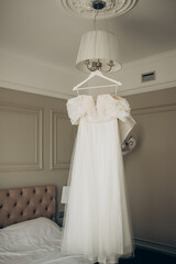 Wedding Elegance: The White Bridal Gown Hanging from the Bedroom Chandelier.
A moment of wedding elegance captured as the white bridal gown drapes gracefully from the bedroom chandelier on the big day