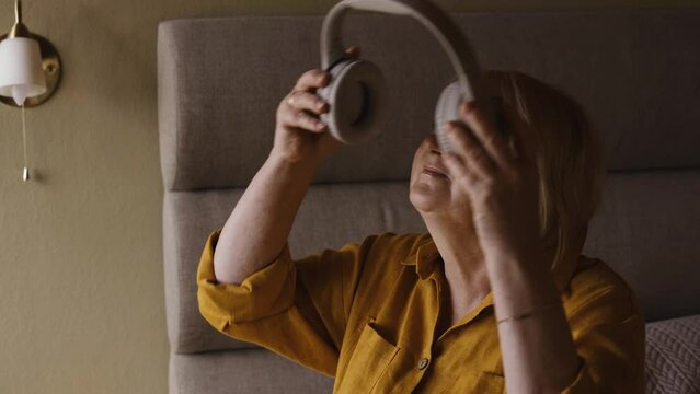 An elderly positive woman listens to music with headphones, dances, then takes off her headphones. Close-up.