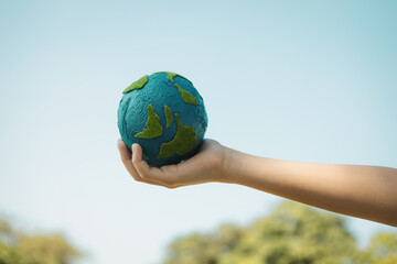 Young boy's hand holding planet Earth globe with sky and cloudscape background as Earth day to save this planet with ESG principle and environment friendly energy for brighter future. Gyre