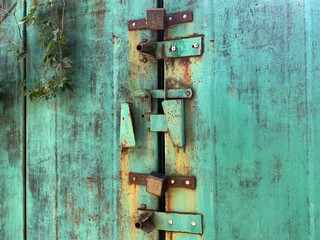 Old green rusty garage door with padlocks, screw locks and heavy handles