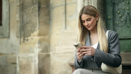 Portrait of young blond woman hold smartphone scrolling social media texting browsing online at urban city Pretty female relax enjoying great day and looking at camera at street outdoors - Powered by Adobe