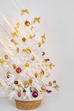 Christmas tree in a wicker basket decorated shiny and gold decorations, bows, balls, toys and with luminous garland on light background. Merry Christmas and Happy Holidays!