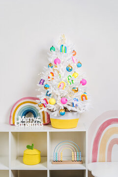 Christmas tree in a wicker basket decorated bright and colorful decorations, rainbow, balls, toys and with luminous garland in children's room. Merry Christmas and Happy Holidays!