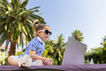 Young fashionable girl sitting next to the swimming pool and using laptop. Technology and summer...
