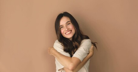Come into my arms. Adorable happy girl with brown hair in t shirt gesturing come here for free hugs and smiling sincerely with welcoming expression isolated on beige background. Come to me, hug self.