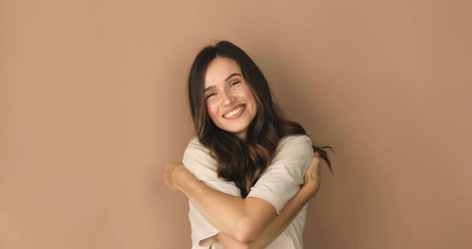 Come into my arms. Adorable happy girl with brown hair in t shirt gesturing come here for free hugs and smiling sincerely with welcoming expression isolated on beige background. Come to me, hug self.