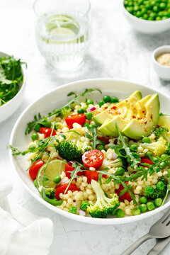 Couscous salad with broccoli, green peas, tomatoes, avocado and fresh arugula. Healthy natural plant based vegetarian food for lunch, israeli cuisine
