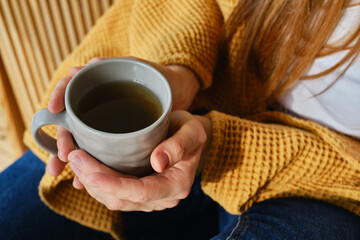 A cup of tea or coffee in the hands of a girl. In the morning the girl drinks hot tea. Enjoy the comfort of home. Close-up of a cup in the hands of a woman in the sun. Warmth and comfort