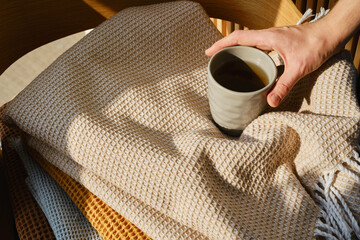 A stack of folded warm blankets of different colors and cup of tea. Cotton blankets. Warm modern textile closeup. Cozy time