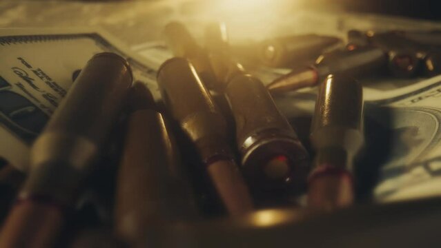 Live ammunition is mixed with dollar bills. Cartridges and money in the beams of a searchlight. The concept of the sale of weapons under lendlease, help with weapons, hired work in the army.