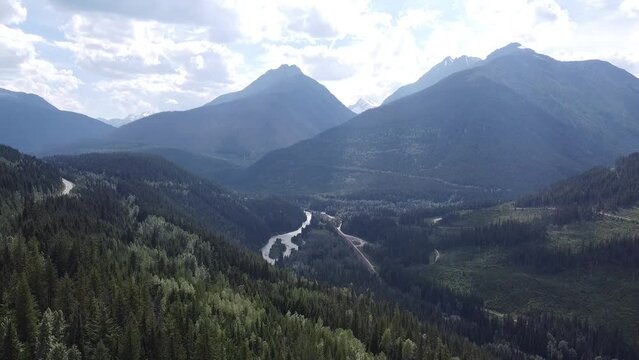 Epic Breathtaking in Slow Motion! Stunning aerial landscape: a valley nestled between majestic mountains, with a crystal-clear lake reflecting the surrounding beauty, encompassed by lush green trees.
